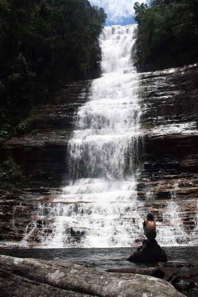 un uomo dall'aspetto molto piccolo accanto a una grande cascata in Venezuela 